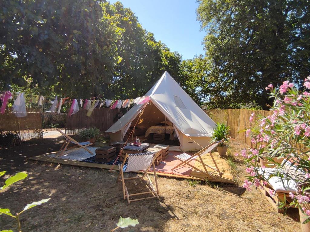 une tente blanche dans une cour avec des chaises et une clôture dans l'établissement Le Bivouac, à Cabariot