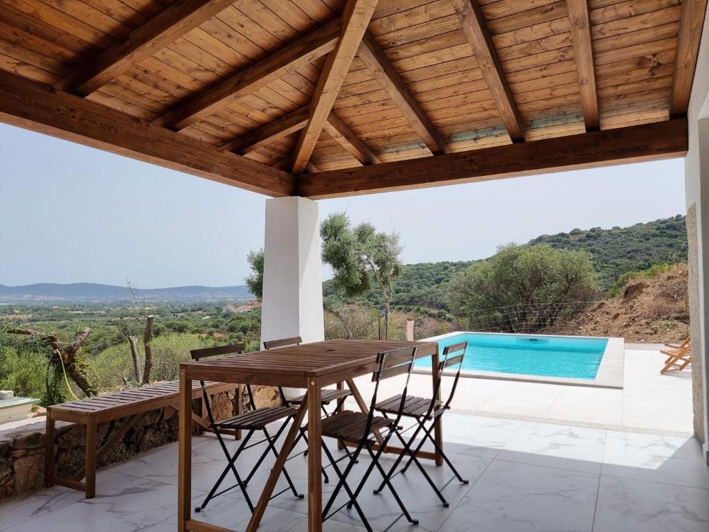 une table et des chaises en bois sur une terrasse avec piscine dans l'établissement Le Ville Del Colle, à Budoni