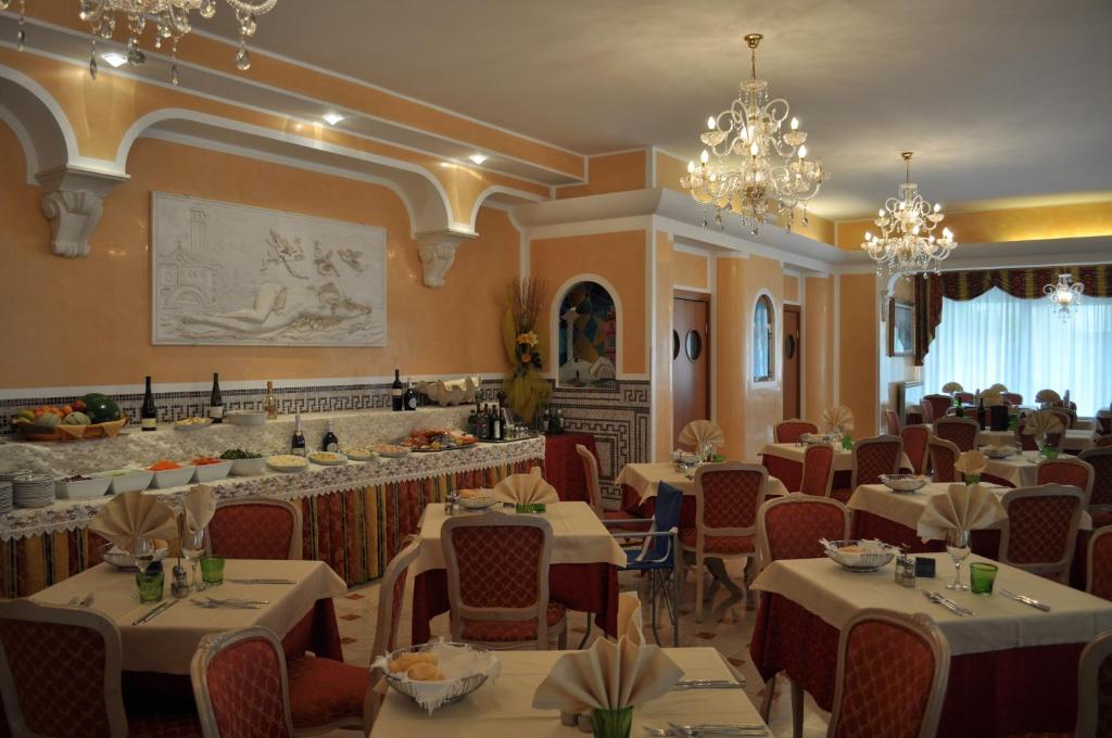 un restaurant avec des tables et des chaises blanches et des lustres dans l'établissement Hotel Real, à Sottomarina