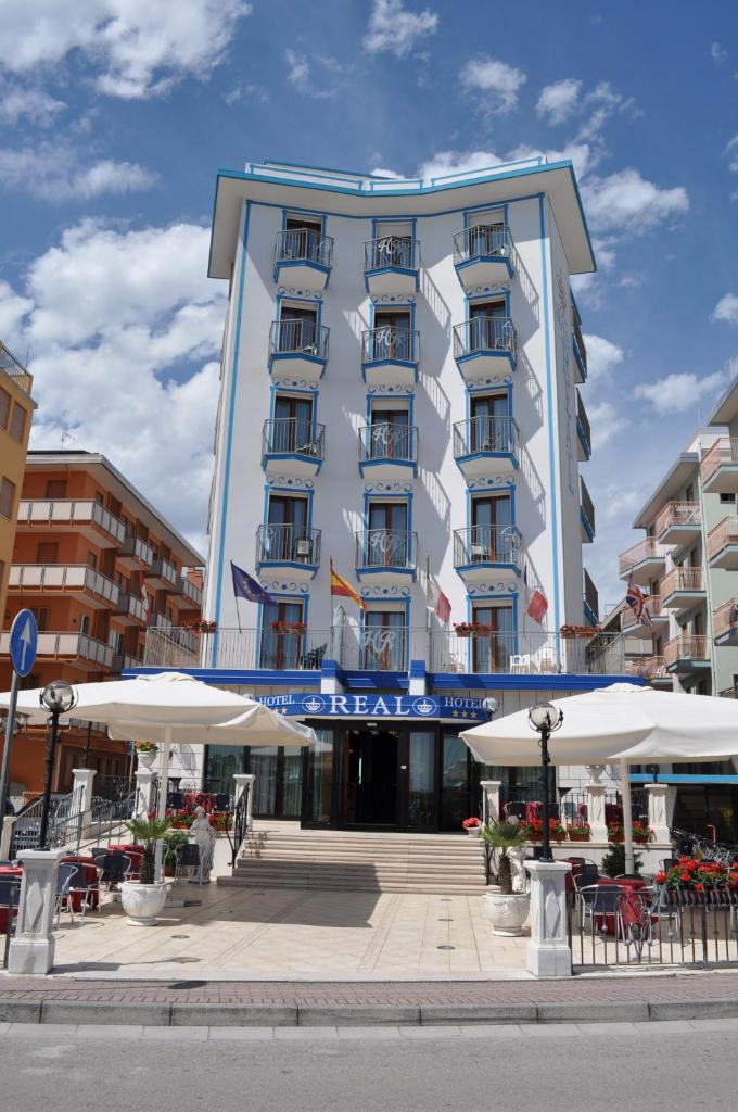 un hôtel avec des tables et des parasols devant lui dans l'établissement Hotel Real, à Sottomarina