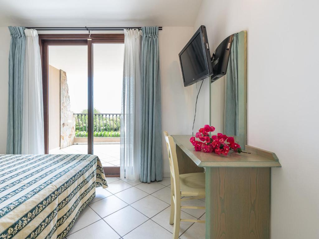 une chambre avec un lit et un bureau avec une télévision dans l'établissement Palm Village, à Villasimius