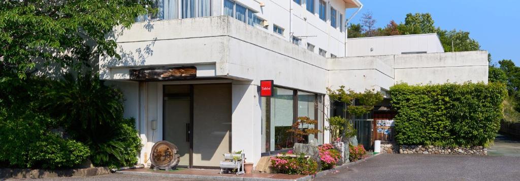 un bâtiment blanc avec un chat assis à l'extérieur dans l'établissement Tabist Setouchinoyado Takehara Seaside, à Takekara