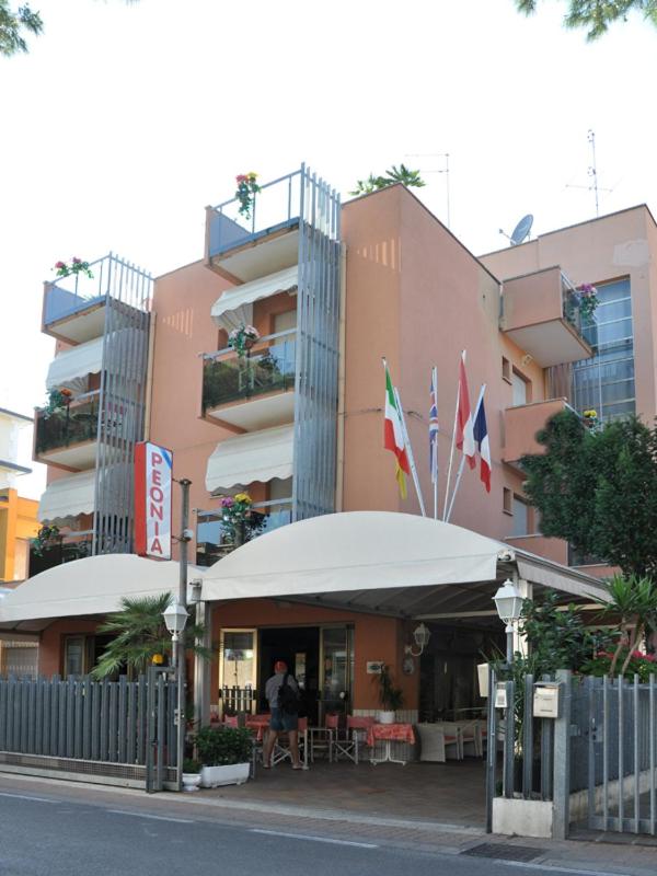 un bâtiment doté d'un restaurant avec drapeaux devant lui dans l'établissement Hotel Peonia, à Rimini