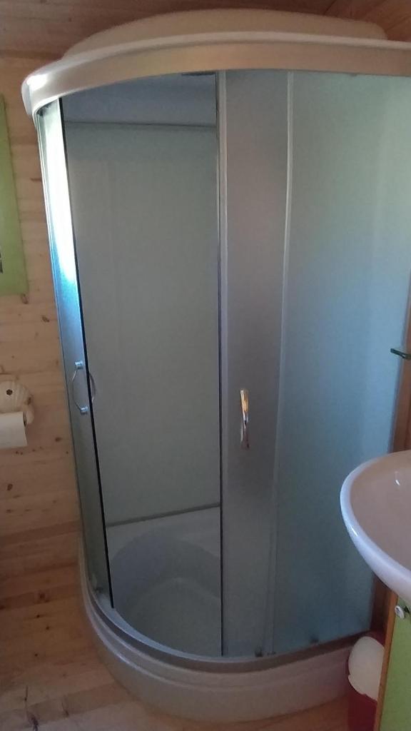 une douche avec une porte vitrée à côté d'un lavabo dans l'établissement Roulotte de la Petite Beauronne, à Les Lèches