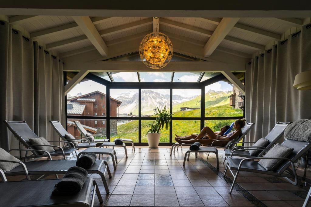 une femme assise sur des chaises dans une pièce avec une grande fenêtre dans l'établissement Résidences Village Montana by Les Etincelles, à Tignes