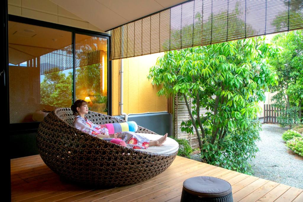 une femme assise dans une chaise en osier sur une terrasse couverte dans l'établissement Yuyado Ichibanchi, à Atami