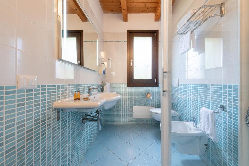 La salle de bains est pourvue de carrelage bleu, d'un lavabo et de toilettes. dans l'établissement Palm Village, à Villasimius
