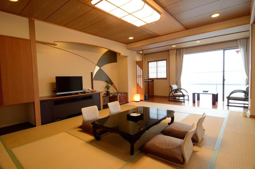 un salon avec une table, des chaises et une télévision dans l'établissement Inatori Tokai Hotel Yuen, à Higashiizu