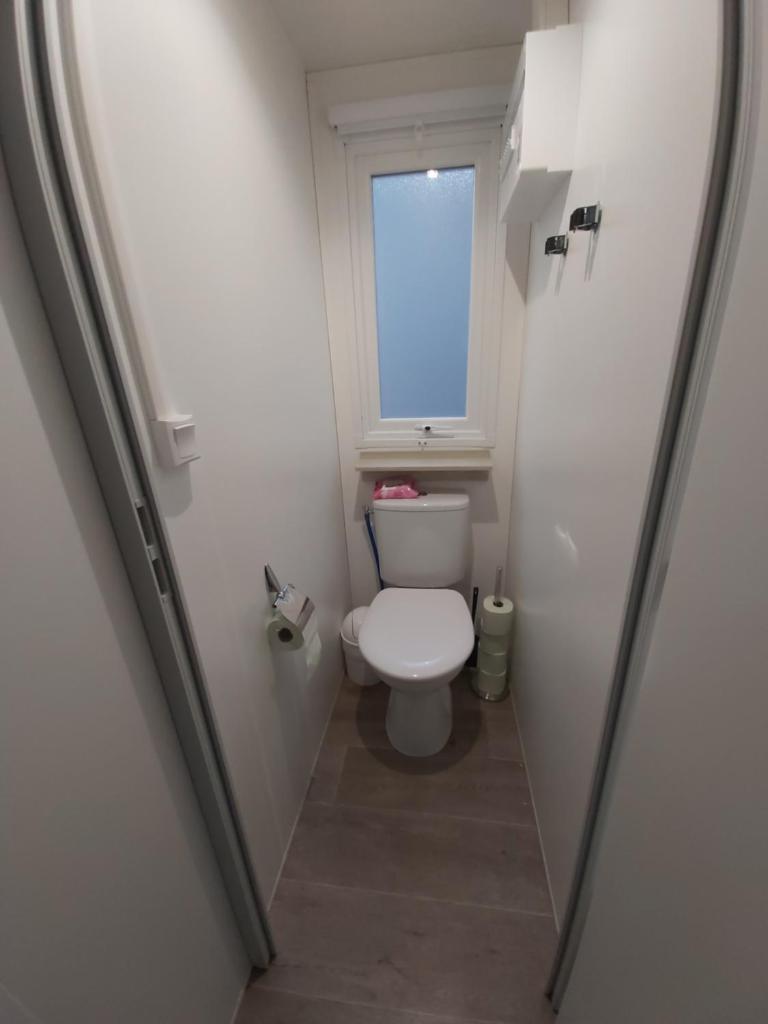 Elle comprend une petite salle de bains pourvue de toilettes et d'une fenêtre. dans l'établissement Mobil home climatisé 6pers. 3CH camping domaine de chaussy 5* Ardèche, à Lagorce 21 autres photos