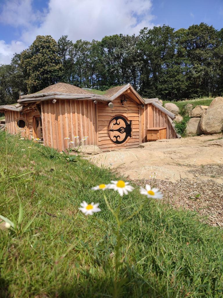 une cabane en bois avec un visage sur la porte et quelques fleurs dans l'établissement La Cabane Korrigans, à Gommené