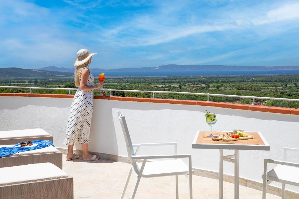 une femme debout sur un balcon tenant une fleur dans l'établissement Lu' Hotel Porto Pino, à SantʼAnna Arresi