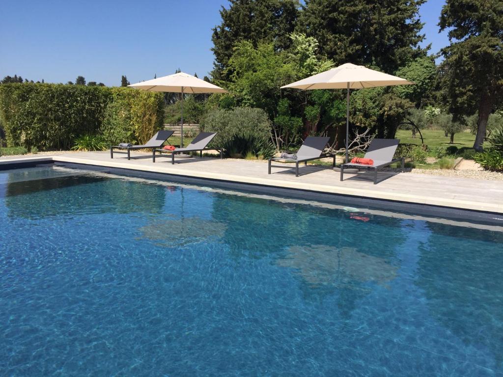 - une piscine avec 2 chaises longues et 2 parasols dans l'établissement Le Mas Terre Des Anges Gite, à Sarrians