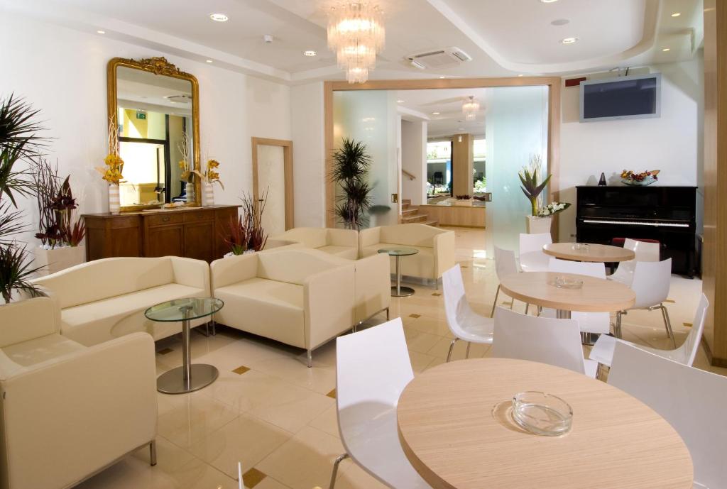 un hall d'entrée avec des meubles et des tables blancs et un miroir dans l'établissement Hotel Olympic, à Misano Adriatico