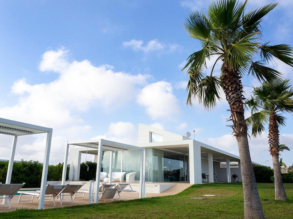 une maison avec des murs de verre et un palmier dans l'établissement Villa Arillà con piscina e padel, à Marina di Ragusa
