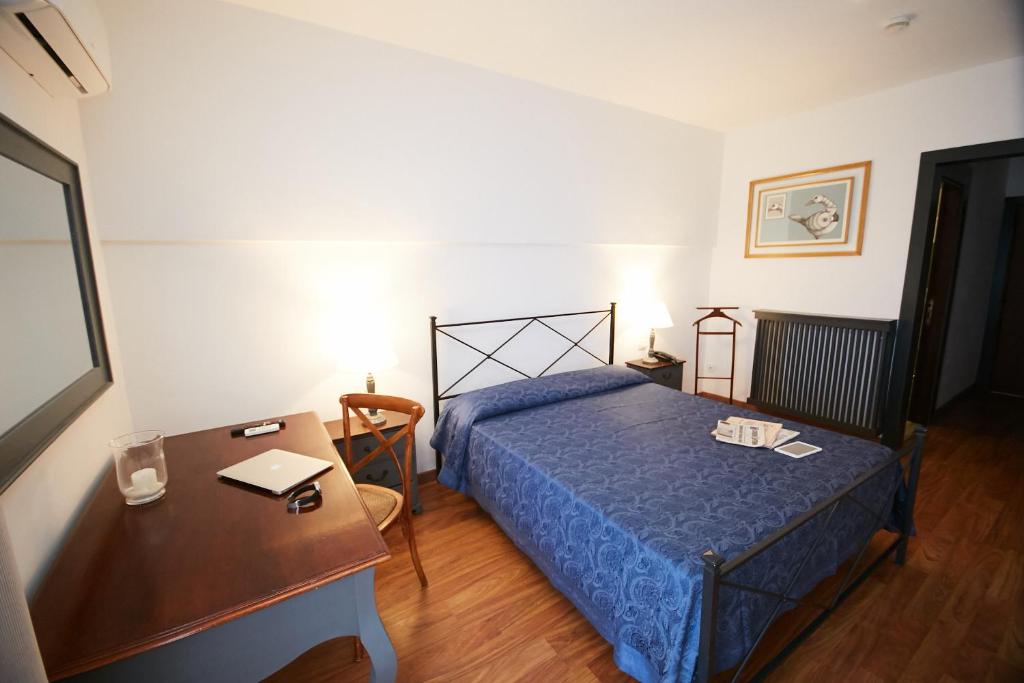 une chambre avec un lit bleu, un bureau et une table dans l'établissement Hotel Enterprise, à Montalto di Castro