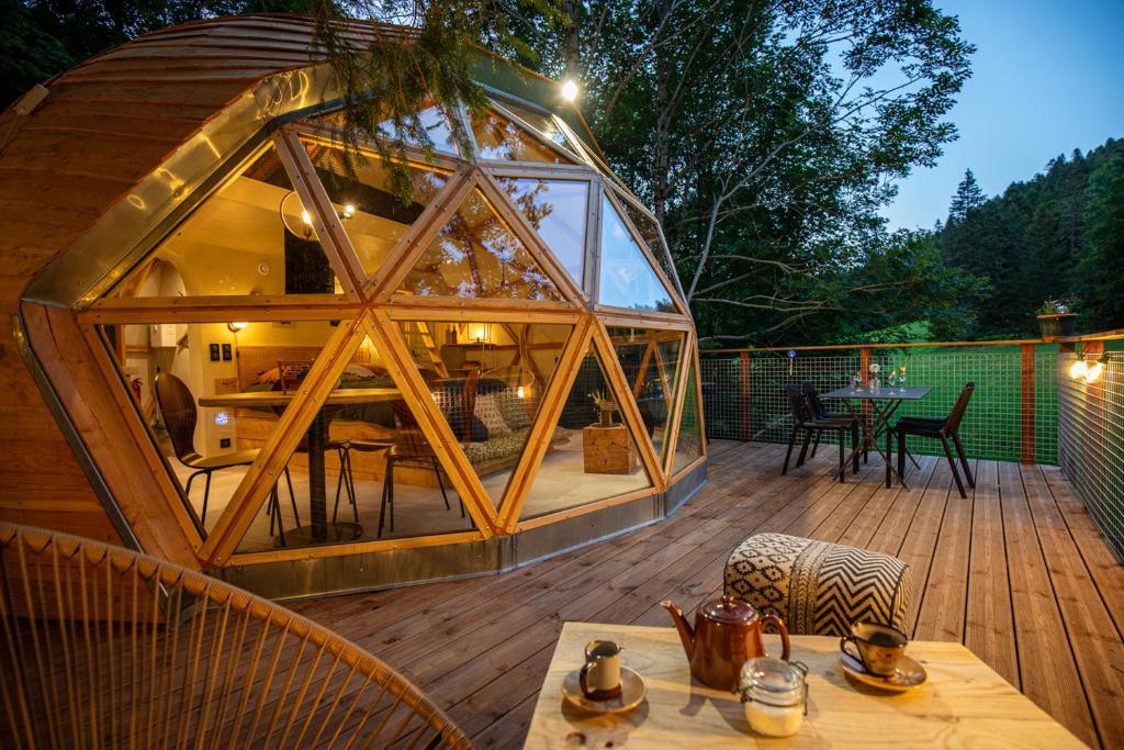 une terrasse en bois avec une grande maison en verre dans l'établissement Dôme panoramique tout confort au cœur du Vercors, à Autrans