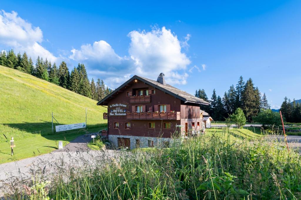 une maison sur une colline avec un champ verdoyant et des arbres dans l'établissement La Vieille Ferme, à Manigod