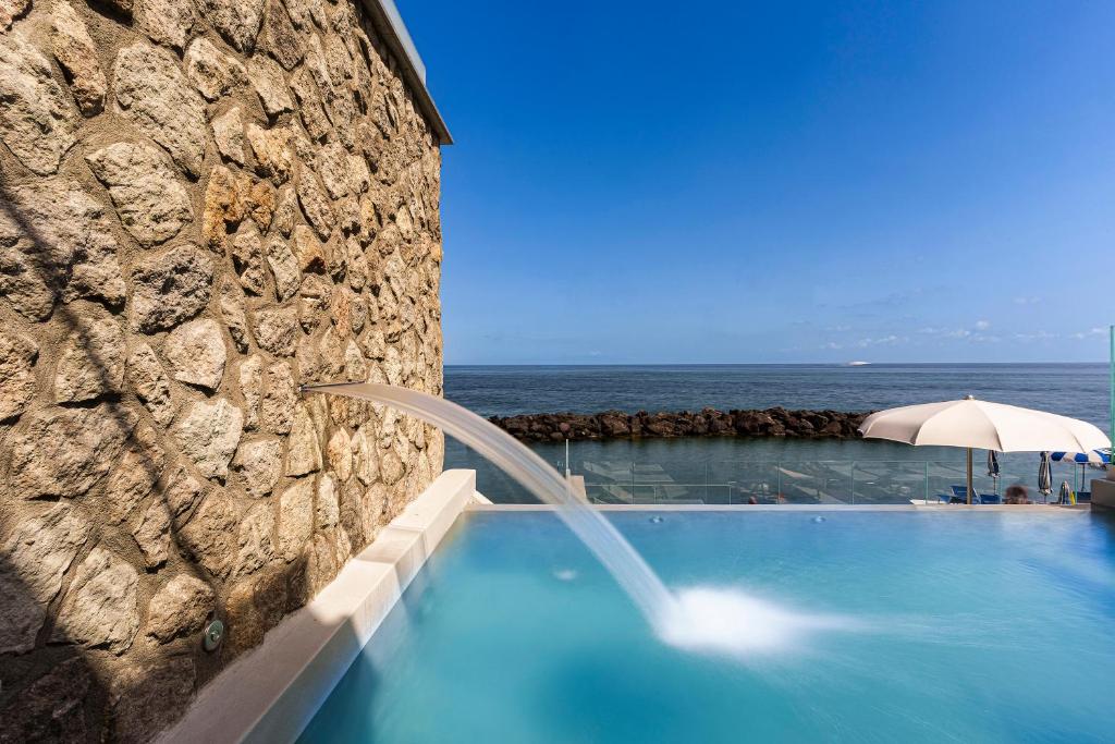- une piscine avec un parasol et l'océan dans l'établissement Ischia Blu Resort, à Ischia