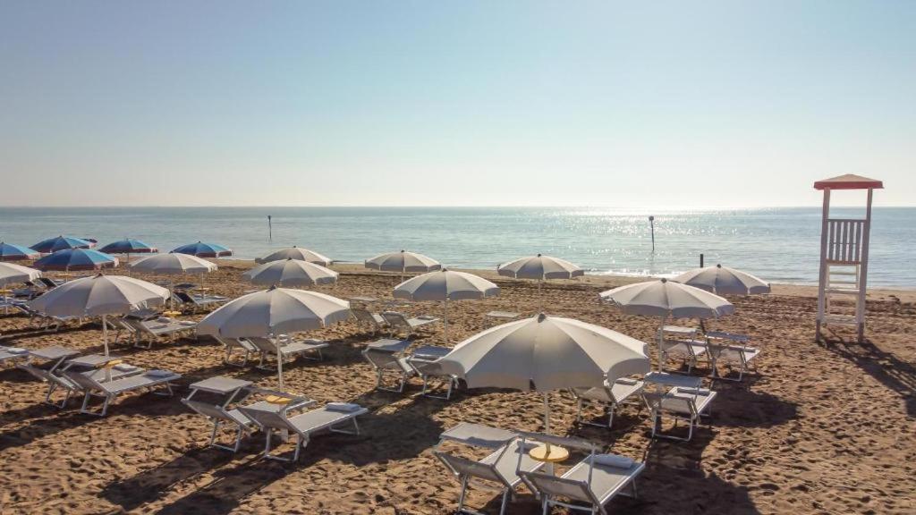 un groupe de chaises et de parasols sur une plage dans l'établissement Hotel Athena, à Lignano Sabbiadoro