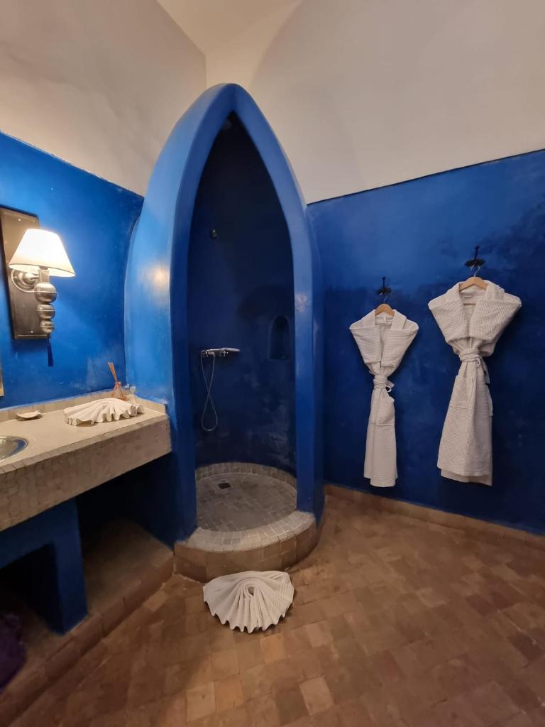 - une salle de bains bleue avec 2 lavabos et des robes sur le mur dans l'établissement Riad Pachavana, à Marrakech