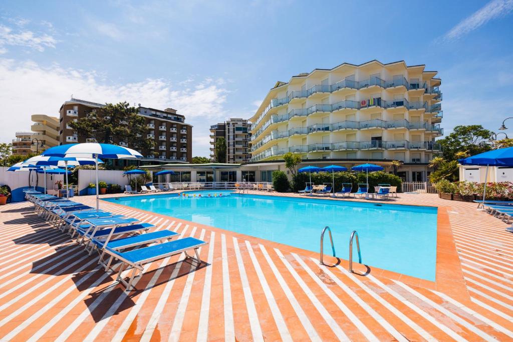 une piscine avec des chaises longues bleues et un hôtel dans l'établissement Hotel Bellevue Beach - sul mare, à Milano Marittima