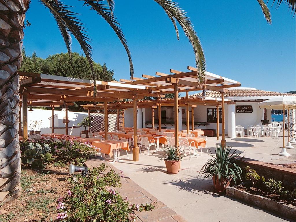un patio avec tables et chaises sous une pergola en bois dans l'établissement Hotel Cala di Mola, à Porto Azzurro