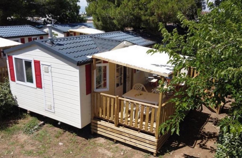 un petit hangar blanc avec une terrasse couverte et une terrasse. dans l'établissement Mobil-Home Camping Novela, à Port-la-Nouvelle