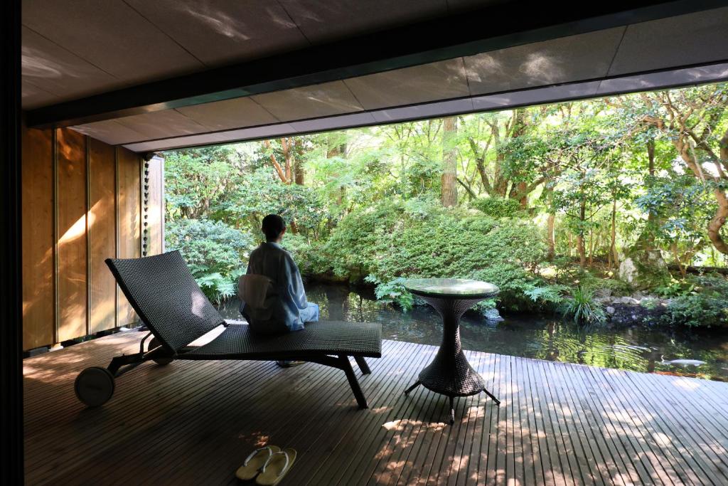 un homme assis sur une chaise sur une terrasse regardant par une fenêtre dans l'établissement Oku Yugawara Tsubaki, à Yugawara