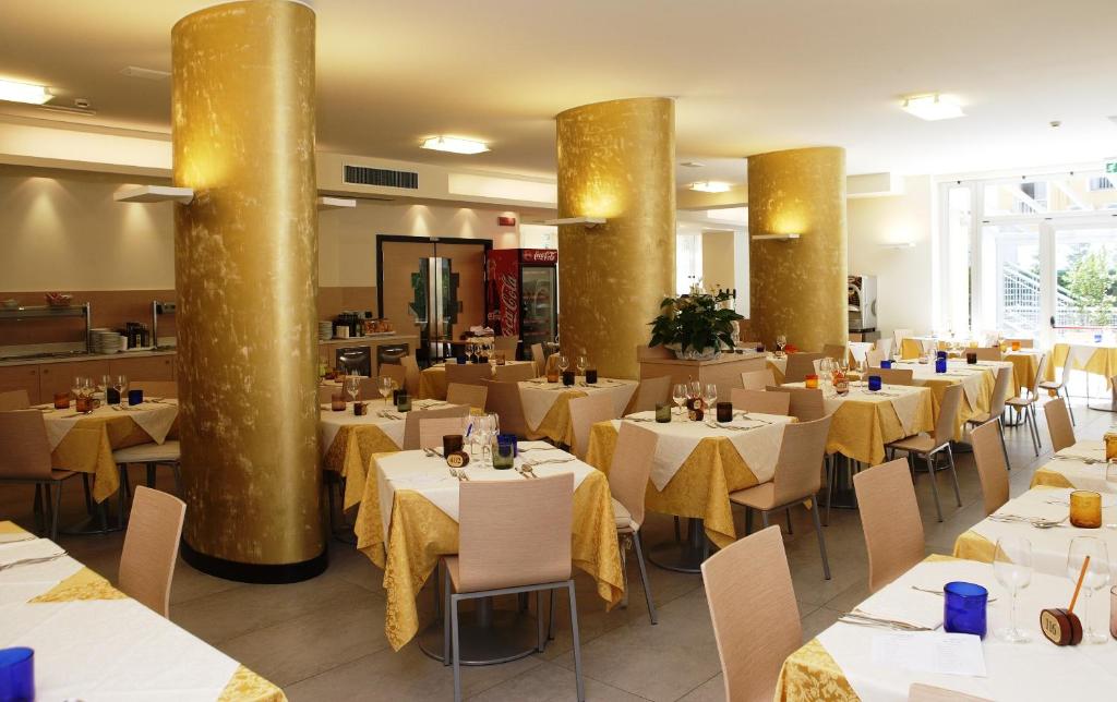 un restaurant avec des tables et des chaises blanches et des colonnes dorées dans l'établissement Eraclea Palace Hotel 4 stelle S, à Eraclea Mare
