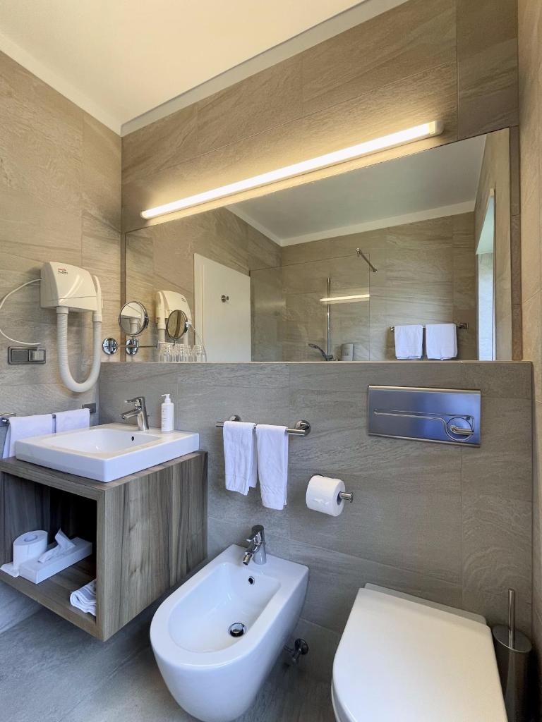 une salle de bain avec un lavabo, des toilettes et un miroir dans l'établissement Hotel Am Wolfgrubenersee, à Soprabolzano