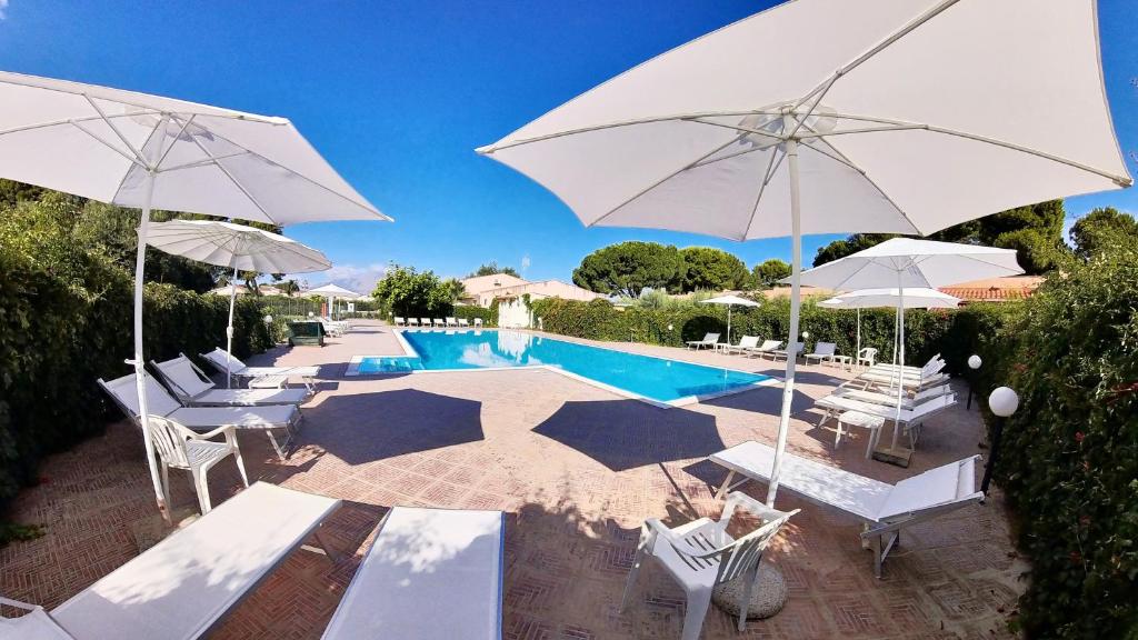- une piscine avec des parasols et des chaises blancs dans l'établissement Villa Teti - Sicilia, à Campofelice di Roccella