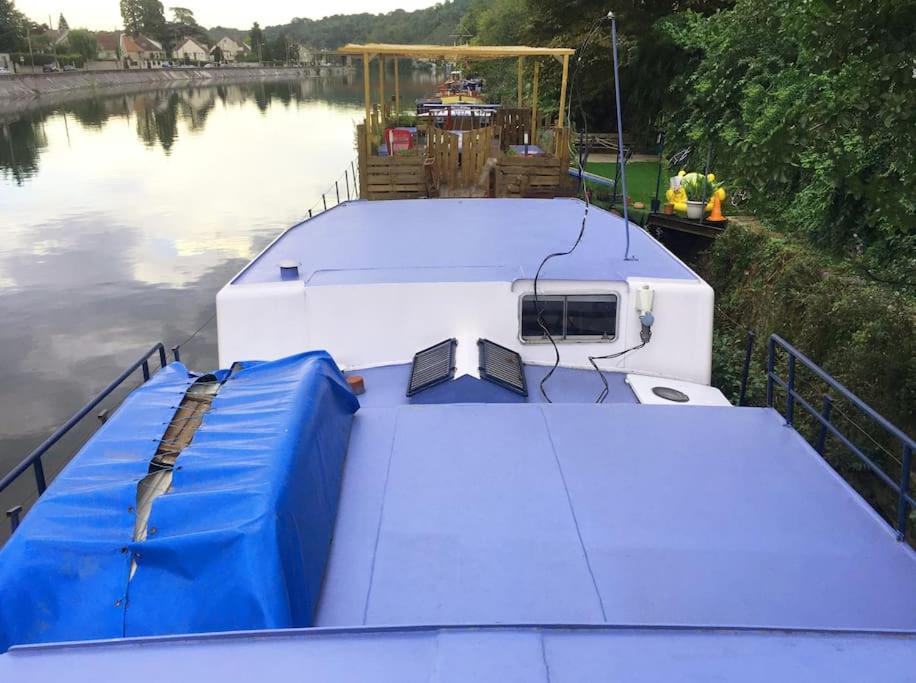 un bateau blanc avec une bâche bleue sur une rivière dans l'établissement Péniche à 25 mn de Paris, à Creil