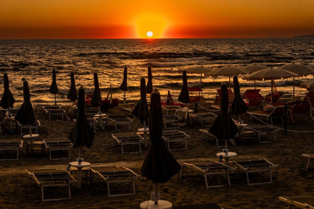 - un groupe de parasols et de chaises sur une plage au coucher du soleil dans l'établissement Hotel Acciaroli, à Acciaroli