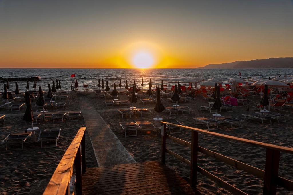 - une plage avec des chaises et des parasols au coucher du soleil dans l'établissement Hotel Acciaroli, à Acciaroli