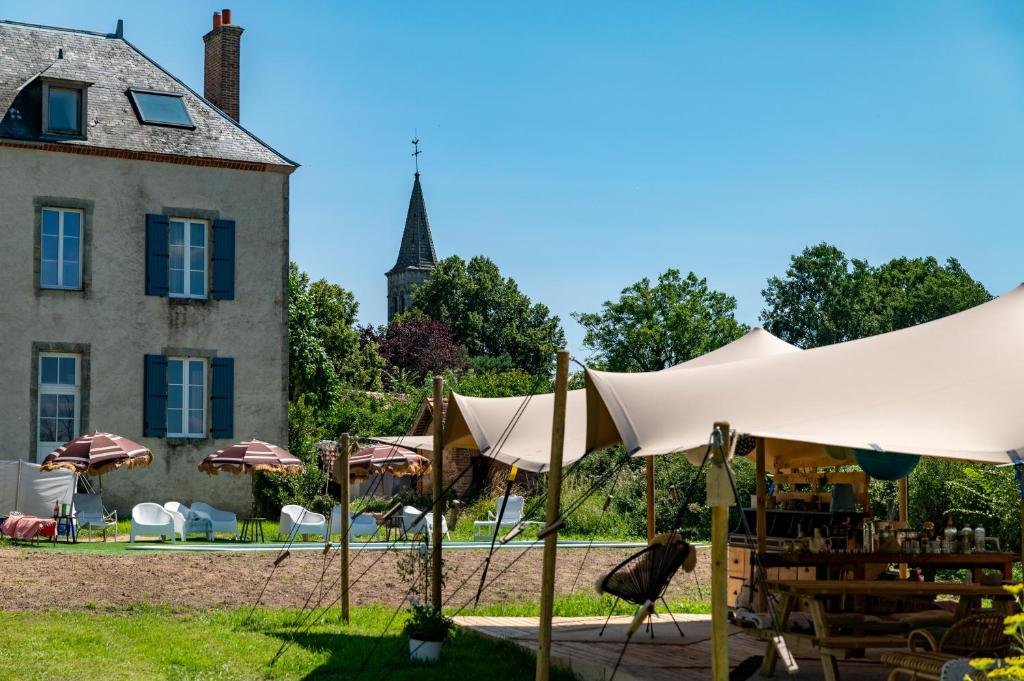 un jardin avec des parasols et un bâtiment avec une église dans l'établissement Le Brasseur Logements - Tents, à Saint-Caprais