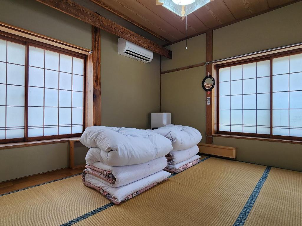 une chambre avec une pile de couvertures dans une chambre avec fenêtres dans l'établissement Minshuku Kojima, à Nozawa Onsen