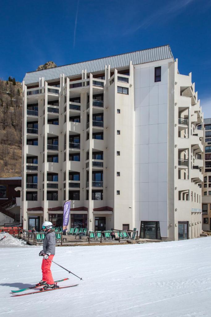 une personne à skis devant un bâtiment dans l'établissement SOWELL HOTELS Le Pas du Loup, à Isola 2000