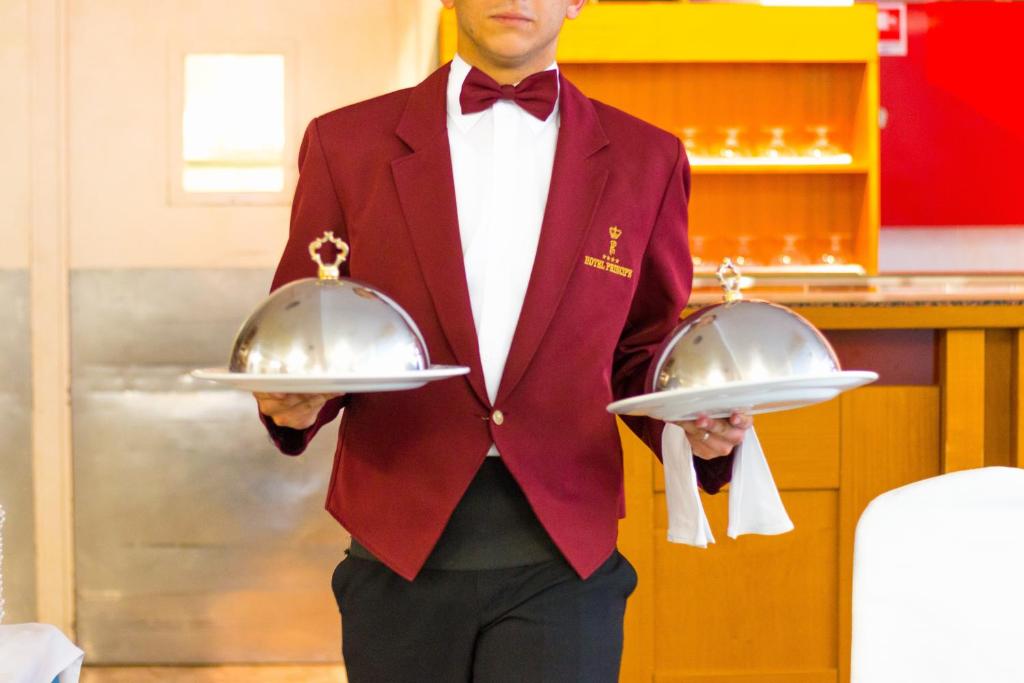 un homme en costume rouge tenant deux plats argentés dans l'établissement Hotel Principe, à Bibione 61 autres photos