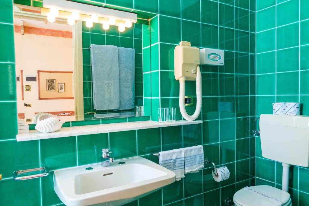 une salle de bain carrelée verte avec un lavabo et un miroir dans l'établissement Hotel Principe, à Bibione