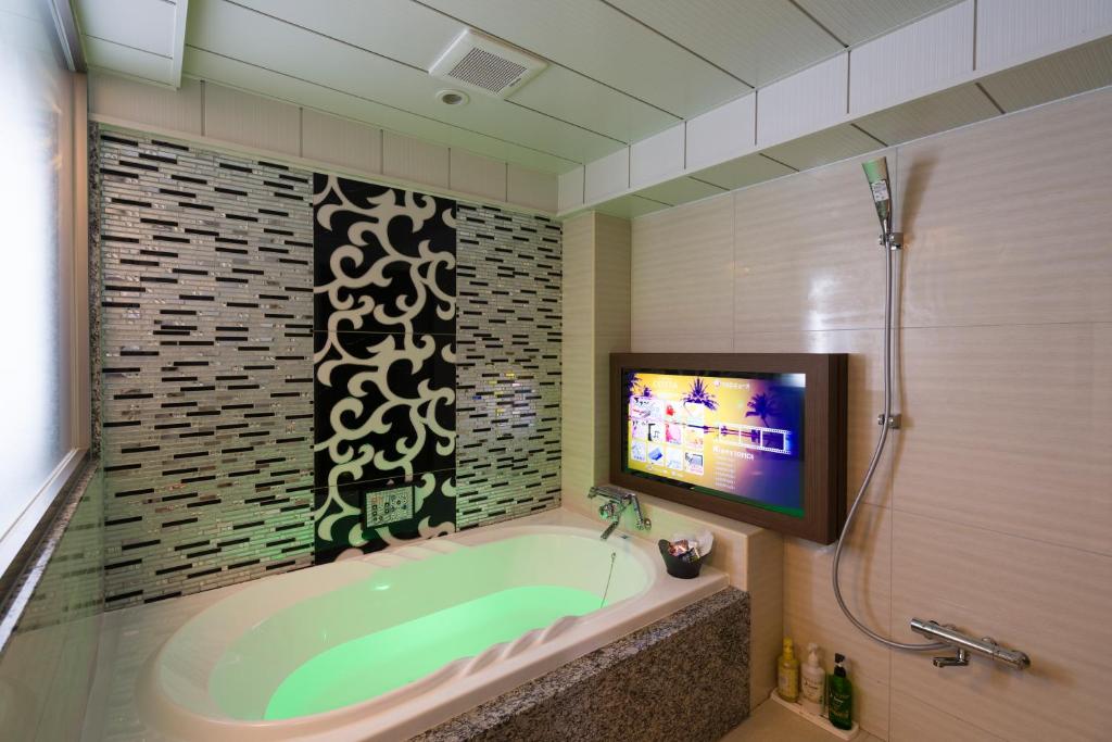une salle de bain avec une baignoire et une télévision dans l'établissement ホテルコスタリゾート飯能, à Hannō