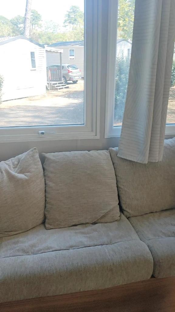 - un canapé avec des oreillers installé devant une fenêtre dans l'établissement Mobil home spacieux, à Seignosse