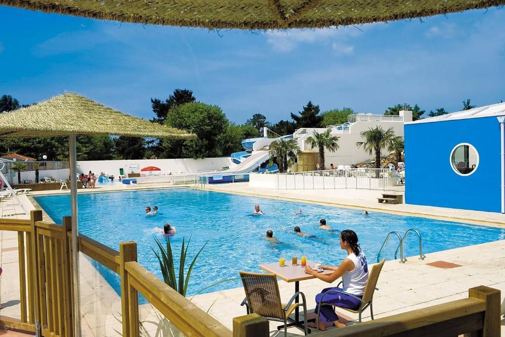 une femme assise à une table devant une piscine dans l'établissement Mobil Home Le Rimbaud - 4/6 pers - 2 ch - 2 sdb, à Saint-Jean-de-Monts