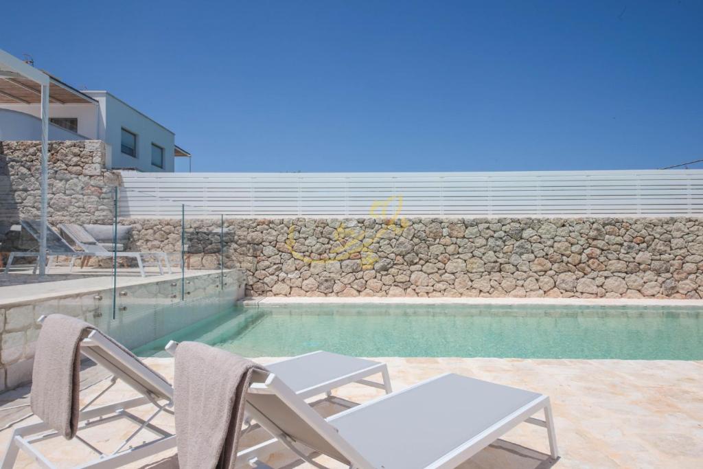une piscine avec des chaises, une table et un mur en pierre dans l'établissement TD Villa Grecale Modern Luxury Villa with Sea View, à Capitolo