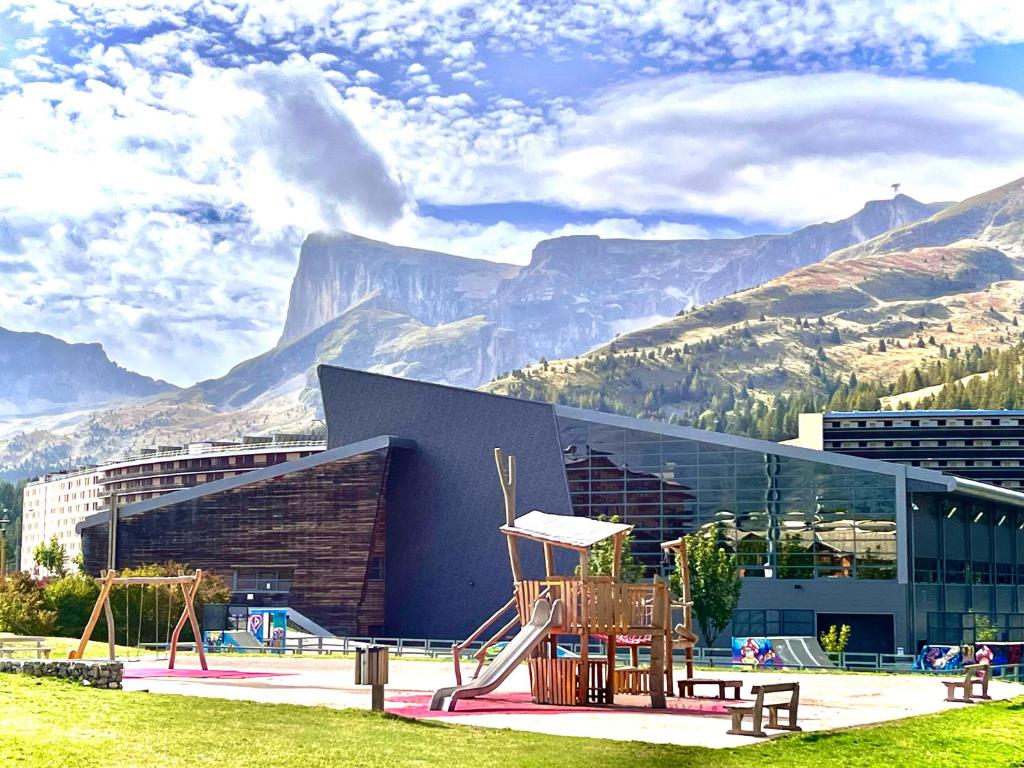 un bâtiment avec une aire de jeux avec des montagnes en arrière-plan dans l'établissement APPARTEMENT CHALETS DU SUPER D, à Saint-Étienne-en-Dévoluy