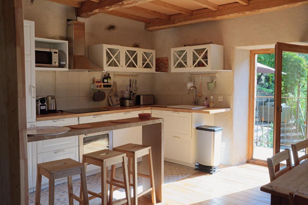 - une cuisine avec des placards blancs et des tabourets en bois dans l'établissement Gite Le MAGNAN au Clarou, à Valleraugue