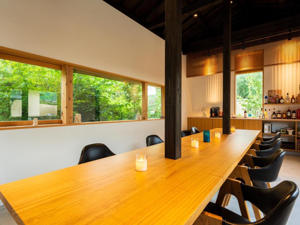 une grande table en bois et des chaises dans une pièce avec des fenêtres dans l'établissement Yufuin Hanarenoyado Yukagetsu, à Yufu