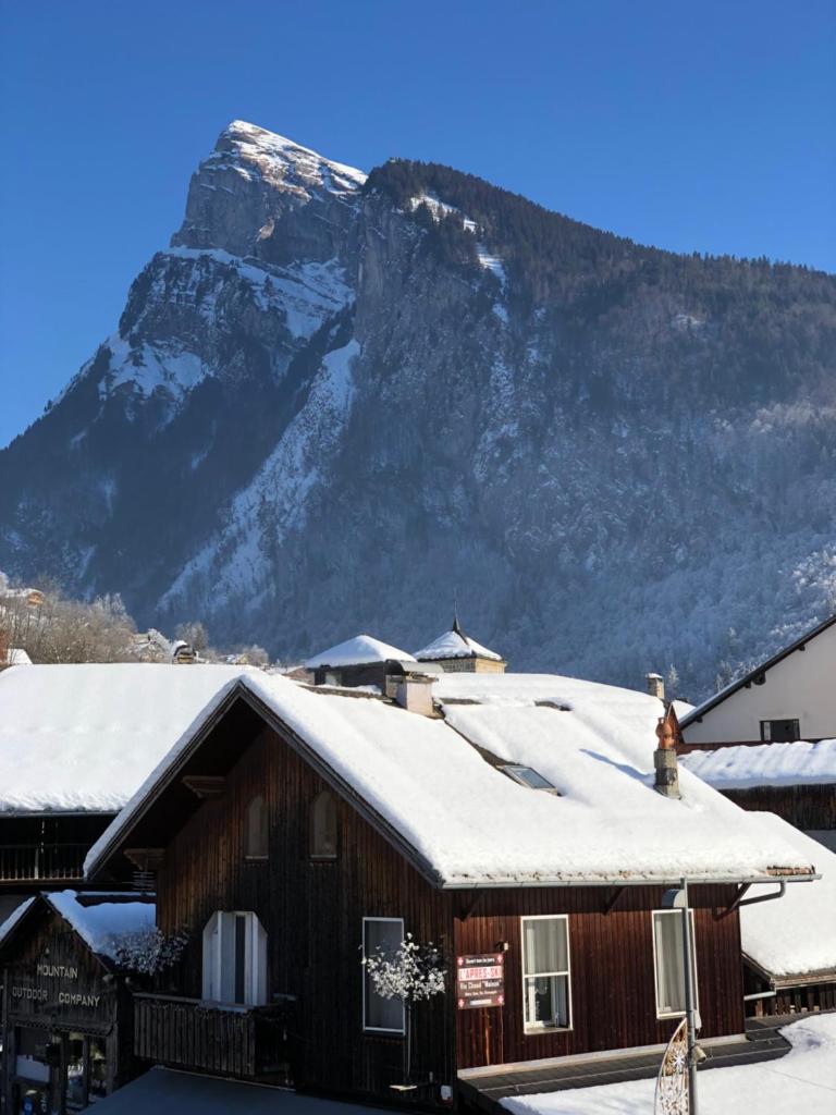 une maison avec une montagne enneigée en arrière-plan dans l'établissement Appartement en hyper centre de Samoëns, à Samoëns