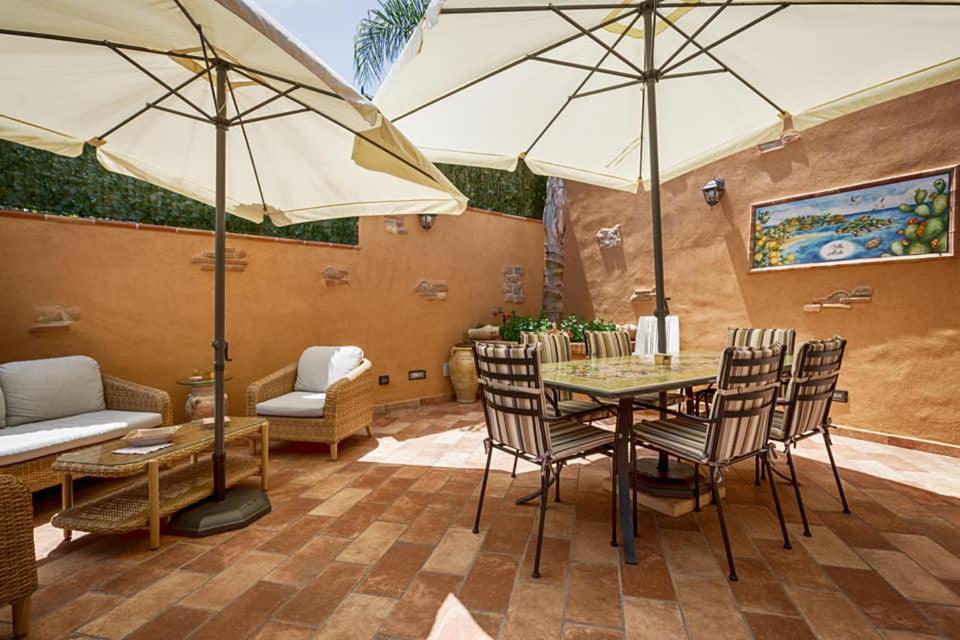 un patio avec une table, des chaises et des parasols dans l'établissement Villa Alecla - Sea Villa near Taormina, à SantʼAlessio Siculo