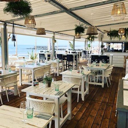 un restaurant avec des tables et des chaises blanches et l'océan dans l'établissement Camping Carabasse Vias plage., à Vias