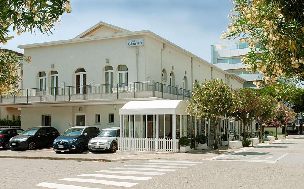 un bâtiment blanc avec des voitures garées devant dans l'établissement Hotel Ginevra, à Lido di Jesolo